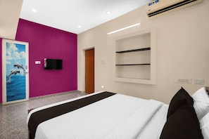 A hotel room with a bed, a television mounted on the wall, a door with a dolphin mural, and a built-in shelf. - Collection O Anbu Nagar Coimbatore (Coimbatore)