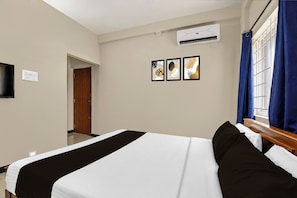 Habitación de hotel con cama, televisor de pantalla plana montado en la pared, equipo de aire acondicionado y ventana con cortinas azules.