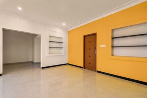 Un passadís amb una porta de fusta, parets blanques i una paret amb un toc de groc.