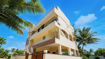 A multi-story building with a flat roof, a balcony on the second floor, and a gated entrance.