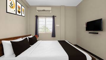 A hotel room with a bed, a television, and a window with curtains.