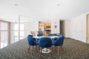 Een vergaderruimte met een glazen tafel en blauwe stoelen, een kitchenette op de achtergrond en uitzicht buiten door grote ramen.