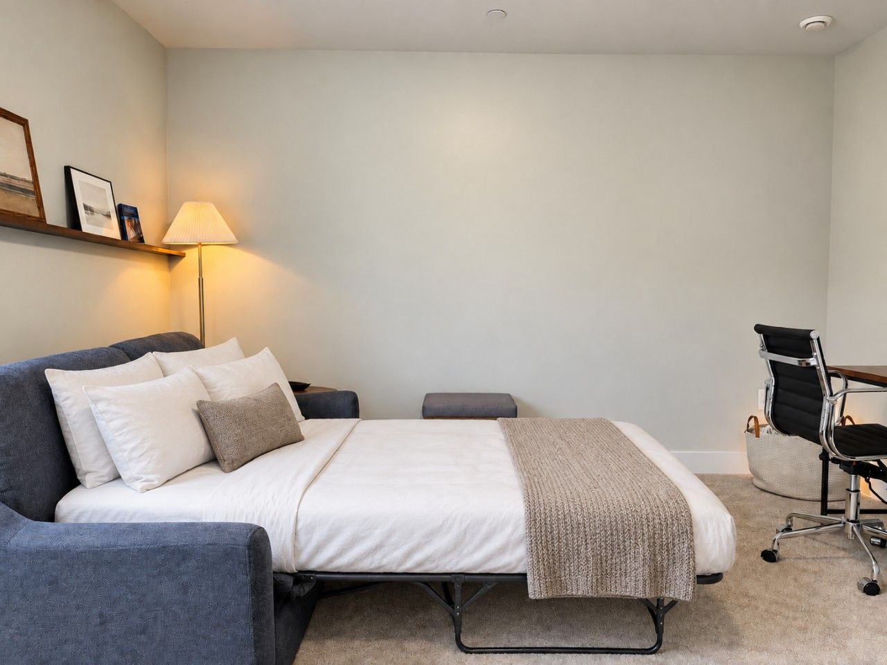 A hotel room with a bed, a desk, a chair, and a lamp.
