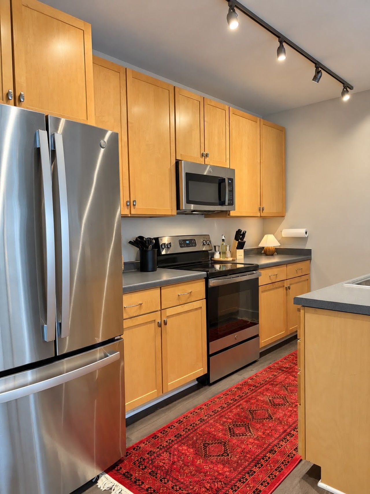 A modern kitchen with stainless steel appliances, wooden cabinets, and a red patterned rug.