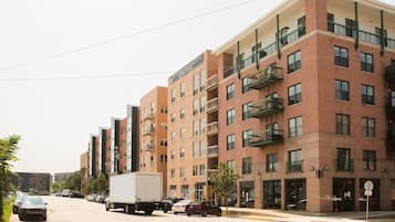 A multi-story building with a brick facade, balconies, and a street view with parked cars and a truck.