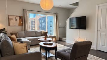 A modern living room with a sofa, armchair, coffee table, and a flat-screen TV.