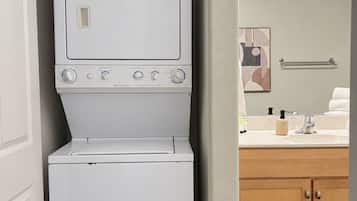 A compact laundry room with a stacked washer and dryer, a wooden cabinet, and a mirror with lights above the sink.