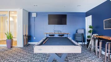 A pool table in a room with blue walls, a mounted TV, and a patterned floor.