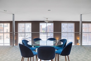A conference room with a glass table surrounded by blue chairs, large windows with a city view, and a ceiling fan. - Third Ward 2BR + Den 2-Story Penthouse | Sleeps 10 (Milwaukee)