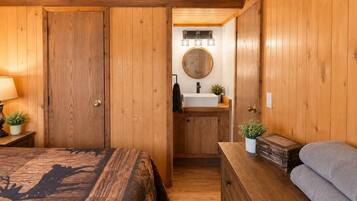 A wooden room with a bed, a dresser, a mirror, and a sink.