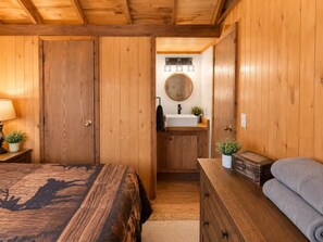 Une pièce en bois avec un lit, une commode, un miroir et un lavabo.