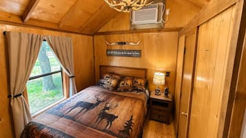 Een slaapkamer in een houten chalet met een bed met patronen van herten en gewei, een kroonluchter en een wandairconditioning.