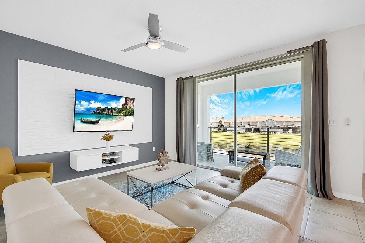 A modern living room with a large flat-screen TV mounted on the wall, a sofa, a coffee table, and a ceiling fan.