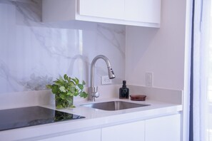 Een keuken met een wit aanrecht, een roestvrijstalen spoelbak en een moderne kraan, plus een potplant.