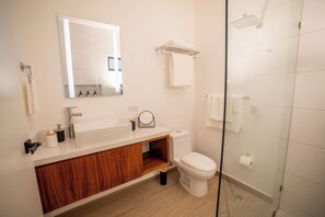 A modern bathroom with a white sink, wooden vanity, a toilet, and a glass shower enclosure. - Vrbo Property (Cabo San Lucas)