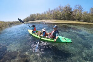 Deux personnes pratiquent le kayak sur une rivière aux eaux claires, entourée d’arbres.