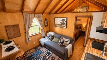 Interior acogedor de una cabaña con techo de madera, un sofá con cojines estampados, una mesa de comedor con un posavasos y una alfombra con diseños geométricos.