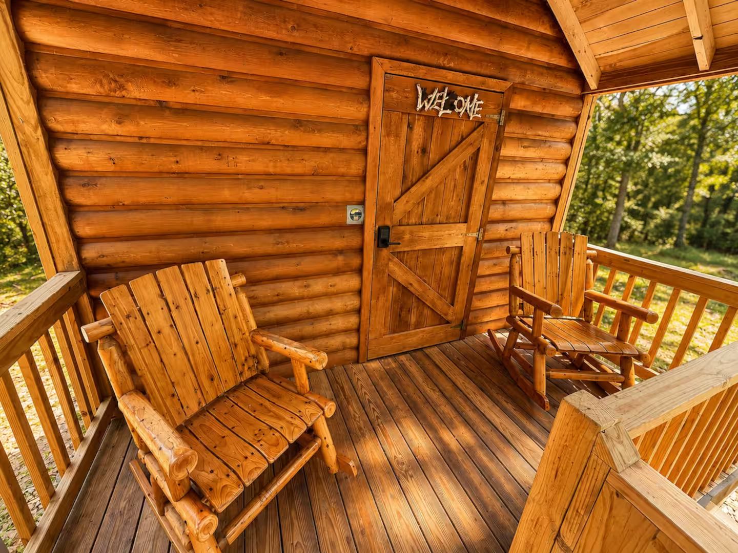 Une cabane en bois avec un porche, une pancarte de bienvenue et deux chaises en bois.