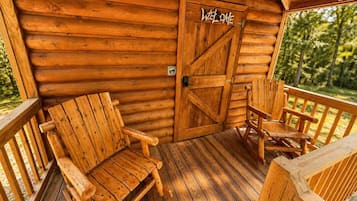 Une cabane en bois avec un porche, une pancarte de bienvenue et deux chaises en bois.
