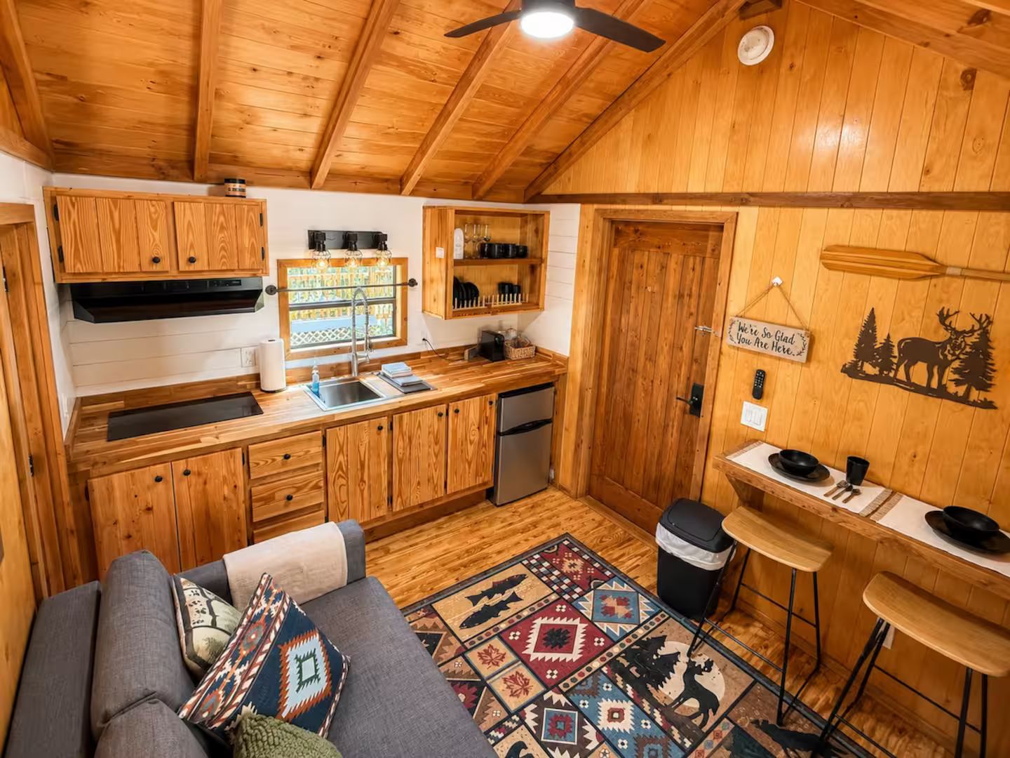 Un intérieur de chalet chaleureux comprenant un coin cuisine, un espace repas et un canapé agrémenté de coussins à motifs.