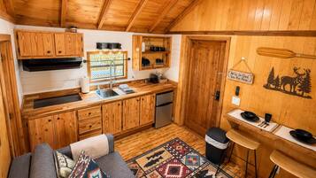 Un intérieur de chalet chaleureux comprenant un coin cuisine, un espace repas et un canapé agrémenté de coussins à motifs.