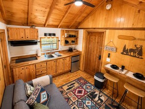 A cozy cabin interior with a kitchenette, a dining area, and a sofa with patterned cushions. - Owl Hollow Cottage - Riverside Escape (Branford)