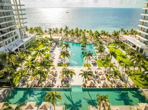 Ein Resort mit einem zentral gelegenen Swimmingpool, umgeben von Palmen und Liegestühlen, mit Blick auf den Ozean.