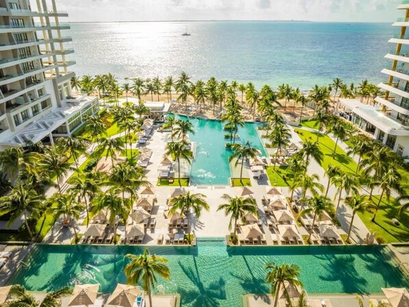 A resort with a central swimming pool surrounded by palm trees and lounge chairs, overlooking the ocean. - Amazing Garza Blanca Resort & SPA Cancun (Cancún)