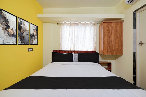 Un dormitorio con cama, un armario de madera, una ventana con cortina de encaje y dos cuadros abstractos en la pared.
