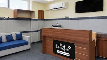 Un área de recepción con un mostrador de madera, un sofá azul y un televisor de pantalla plana montado en la pared.