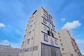 Un edificio de varios pisos con un llamativo elemento vertical, una serie de ventanas y un letrero que indica un punto de servicio o recolección.