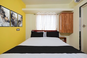 Un dormitorio con cama, un armario de madera, una ventana con cortina de encaje y dos cuadros abstractos en la pared.