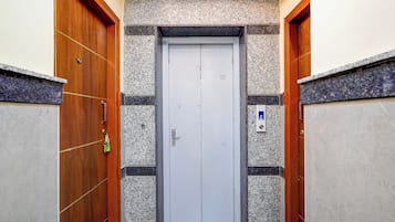Un pasillo estrecho con una puerta de ascensor blanca, flanqueado por puertas de madera y paredes con diseños de baldosas salpicadas.
