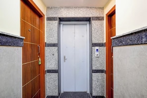 Un pasillo estrecho con una puerta de ascensor blanca, flanqueado por puertas de madera y paredes con diseños de baldosas salpicadas.