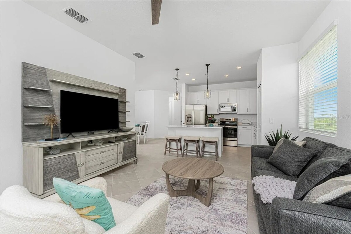 A modern living room with a flat-screen TV, grey sofa, and a dining area with a round table.