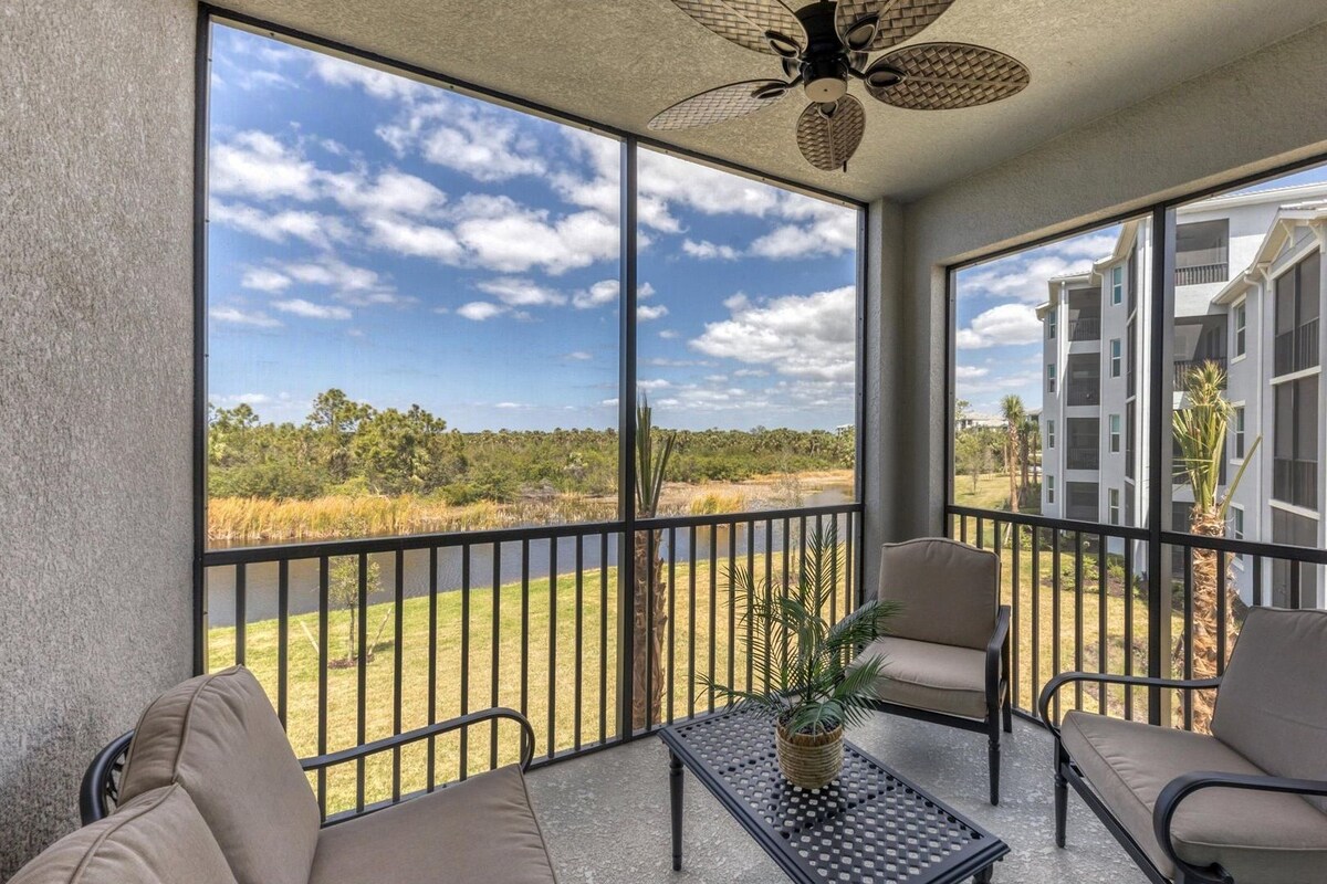 A balcony with a view of a lake and buildings, furnished with chairs and a table.