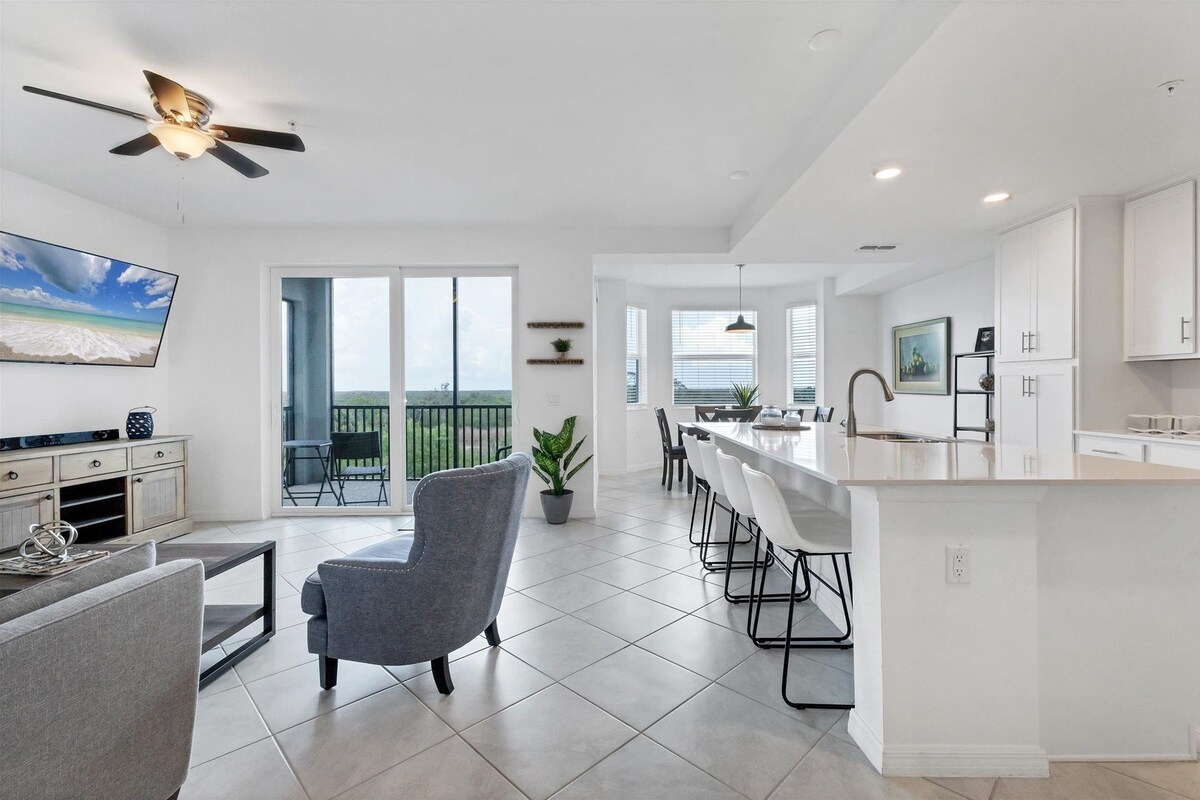 A modern kitchen with a central island, a dining area with a view, and a balcony with a TV.