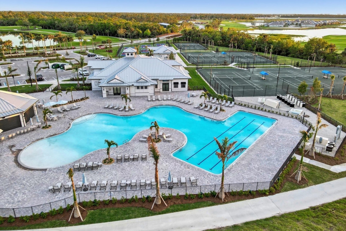 A resort with a large swimming pool, multiple tennis courts, and a golf course in the background.