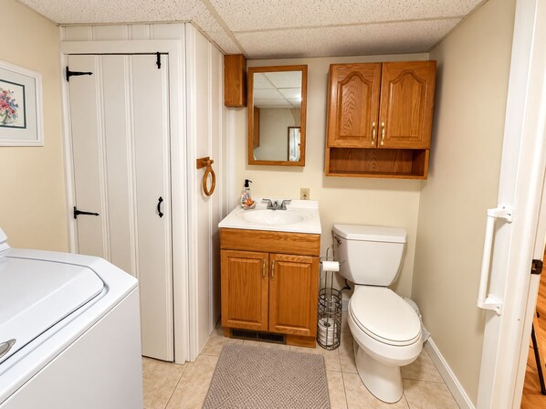 A compact bathroom with a toilet, sink, wooden cabinets, a mirror, and a door with a towel ring.
