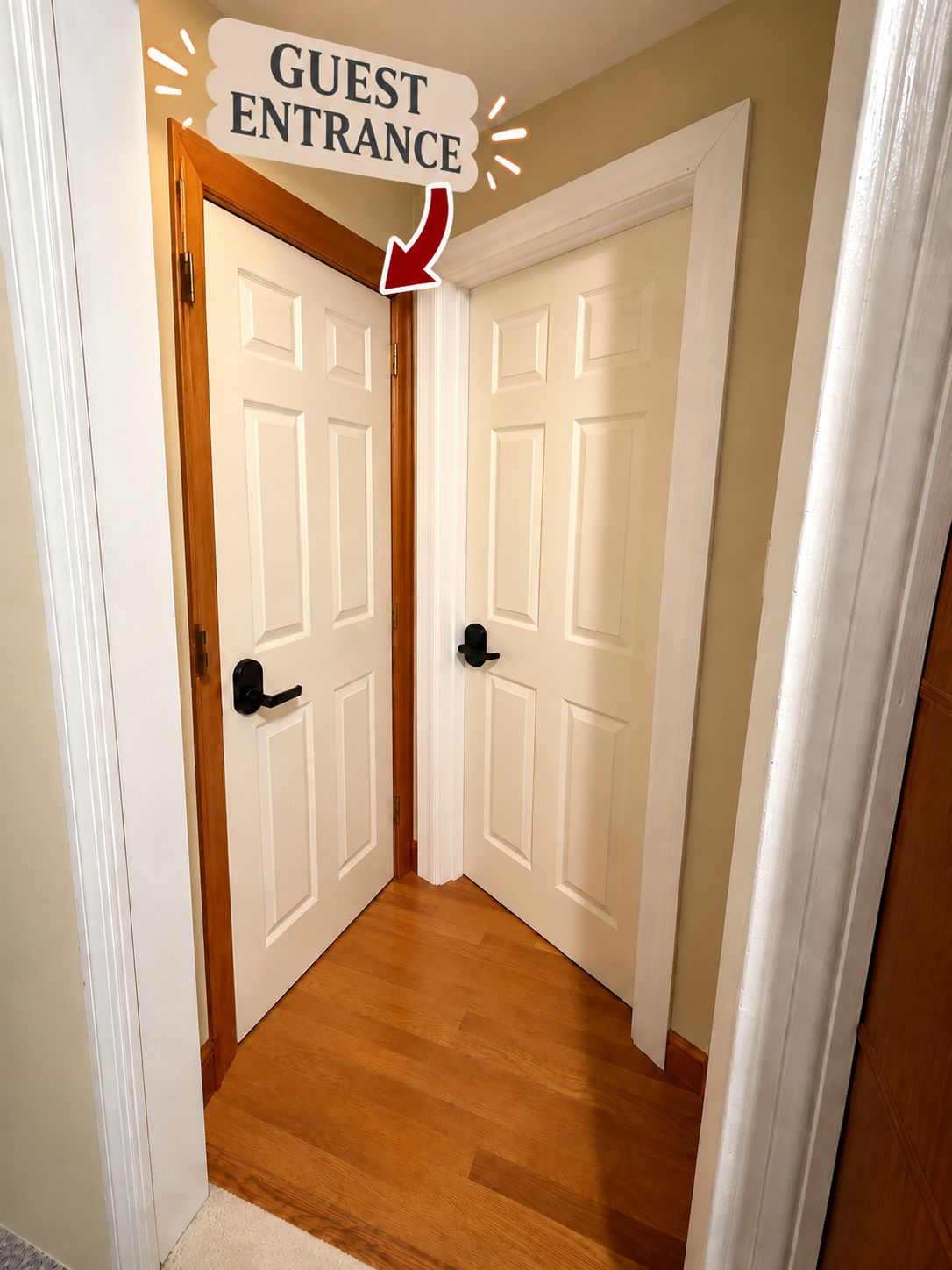 Una entrada para huéspedes con dos puertas blancas, una con marco de madera y la otra con picaporte negro.