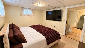Une chambre à coucher avec un lit, un téléviseur fixé au mur et une porte donnant sur une autre pièce.