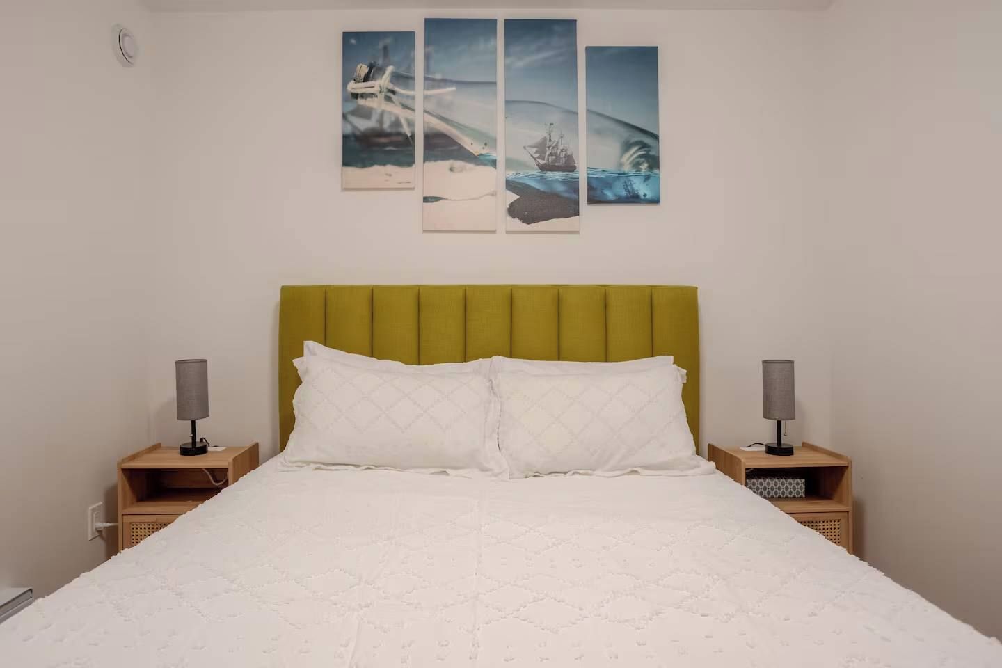 A bed with a green headboard, two bedside tables with lamps, and three wall-mounted paintings.