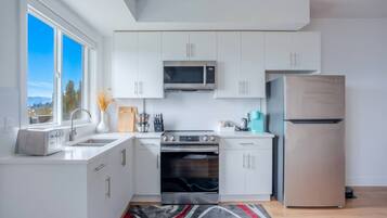 Une cuisine moderne avec des meubles blancs, un réfrigérateur en acier inoxydable, un four à micro-ondes, un grille-pain et une cuisinière.