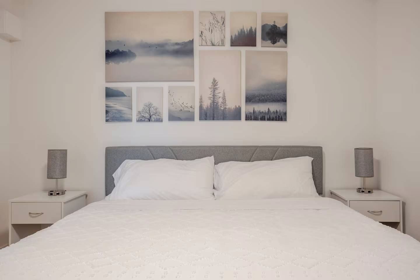Een slaapkamer met een bed, twee nachtkastjes en een muur met zes ingelijste foto's.