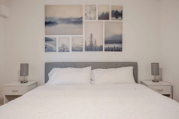 A bedroom with a bed, two bedside tables, and a wall with six framed pictures.