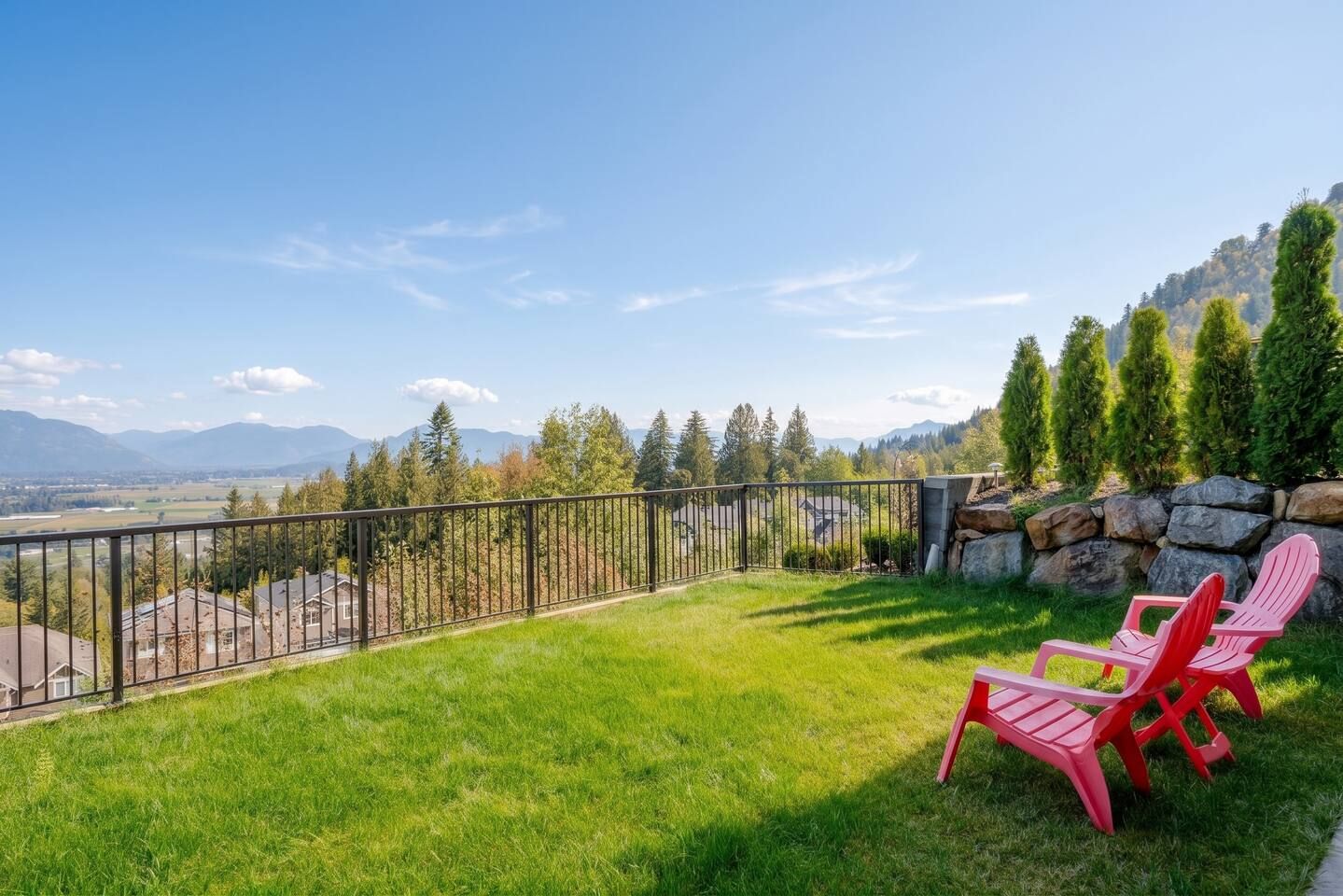 A grassy outdoor area with a metal fence, red chairs, and a view of mountains and trees.
