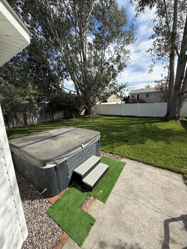 Un patio trasero con un jacuzzi, una terraza de madera y una cerca blanca.