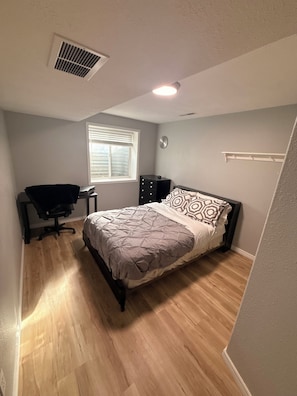 Un dormitorio con cama, escritorio, silla, ventana y reloj de pared.
