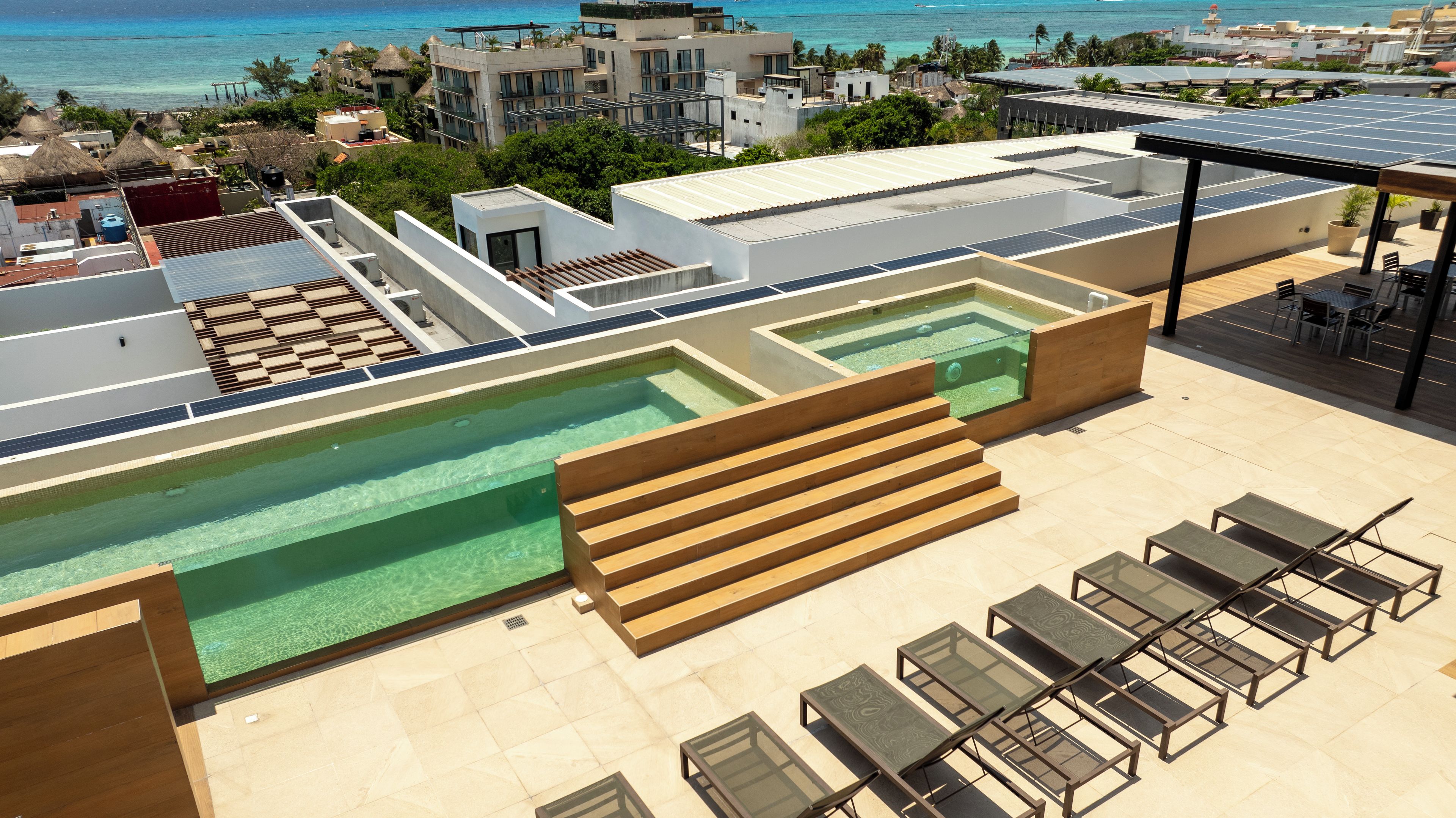 Un espace piscine sur le toit, comprenant plusieurs piscines, des chaises longues et une vue sur l’océan.