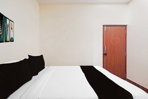 A hotel room with a bed, a wooden door, and a wall with framed artwork. - Collection O Thanisandra Bangalore Surya (Bengaluru)